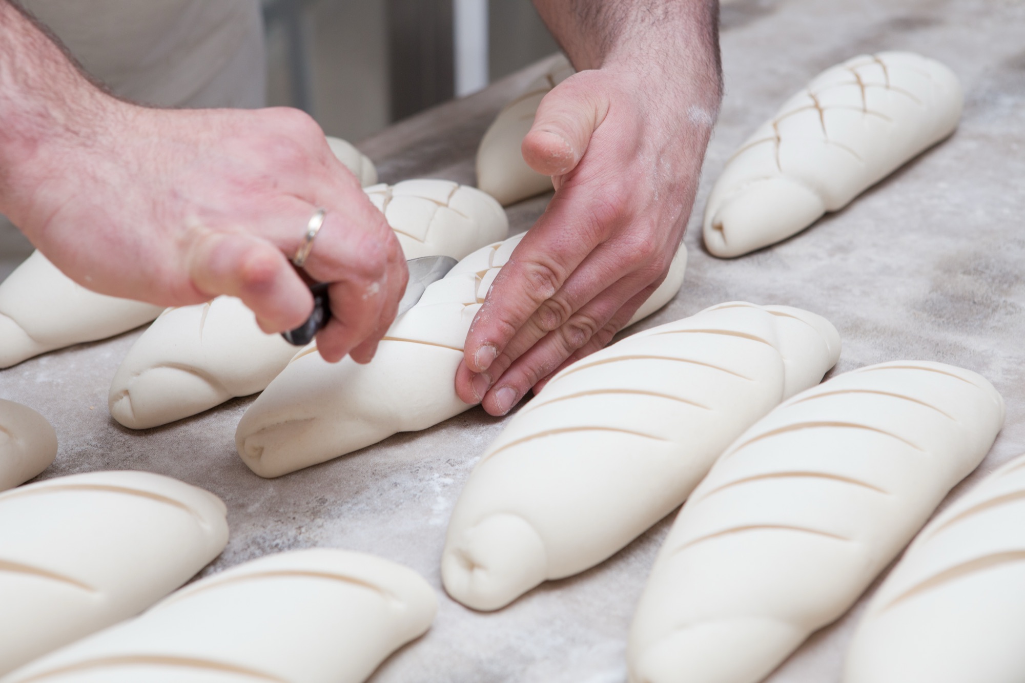 Bäcker schneidet Baguettes vor dem Backen ein